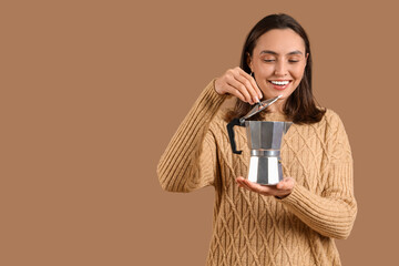 Pretty young woman with geyser coffee maker on brown background