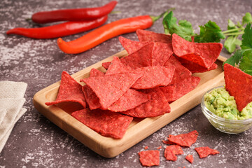 Wooden tray with red nachos, chilli and guacamole on grey grunge background