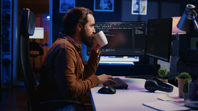 Focused programmer drinking coffee in apartment while solving database errors on computer. Remotely working IT admin concentrated on finalizing coding project in home office, camera B