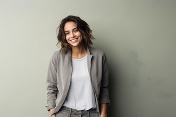 Portrait of a happy young woman standing with hands in pockets against grey background