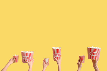 Hands holding buckets with popcorn on yellow background