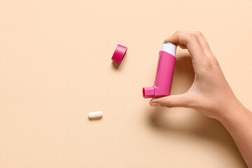 Child's hand with asthma inhaler and pill on beige background