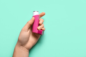 Child's hand with asthma inhaler on turquoise background