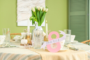Beautiful table setting with flowers for International Women's Day celebration near color wall