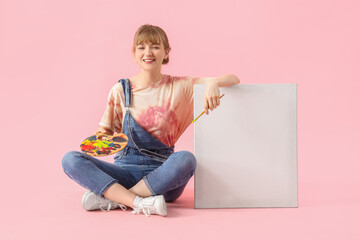 Female artist with paint palette and canvas sitting on pink background