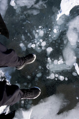 feet standing on frozen lake with methane gas bubbles trapped under ice