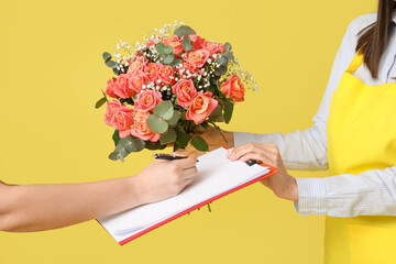 Young delivery woman giving bouquet of beautiful flowers on yellow background