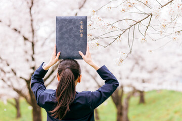 満開の桜の下で卒業証書を頭の上に載せる高校生・女子高生（卒業生・卒業・卒業式）
 - obrazy, fototapety, plakaty