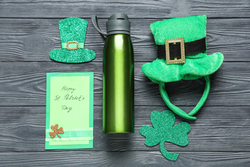 Sports bottle, leprechaun's hats, clover and greeting card on wooden background. St. Patrick's Day...