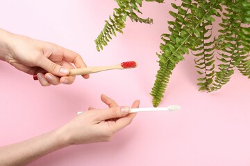 Woman holding natural bamboo and plastic toothbrushes on pink background, top view