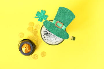 Glass of beer with coins and leprechaun hat on yellow background. St. Patrick's Day celebration
