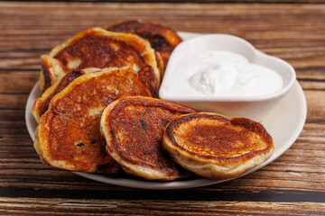 Pancakes with sour cream on the wooden table. Russian fritters oladyi. Close up, rustic, heart shape bowl