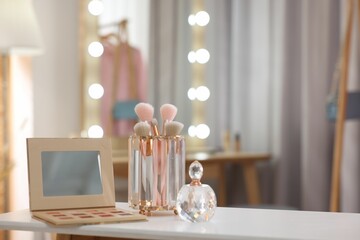 Set of brushes, eyeshadow palette and perfume on white table in makeup room, space for text