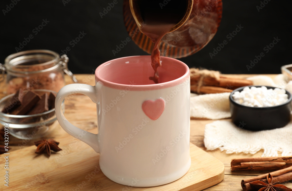 Canvas Prints Pouring tasty hot chocolate into cup at wooden table, closeup