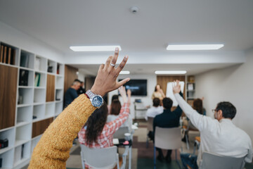 Focused group of people in a workshop setting with raised hands eager to ask questions or provide answers during an interactive session.