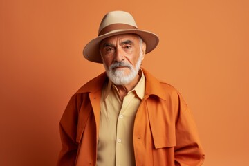 Portrait of a senior man in a hat and coat on a orange background.
