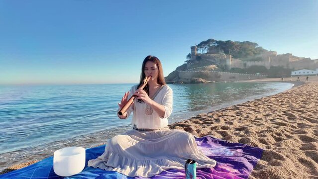 Beautiful caucasean woman playing calm music with native american flute on the beach, 4K