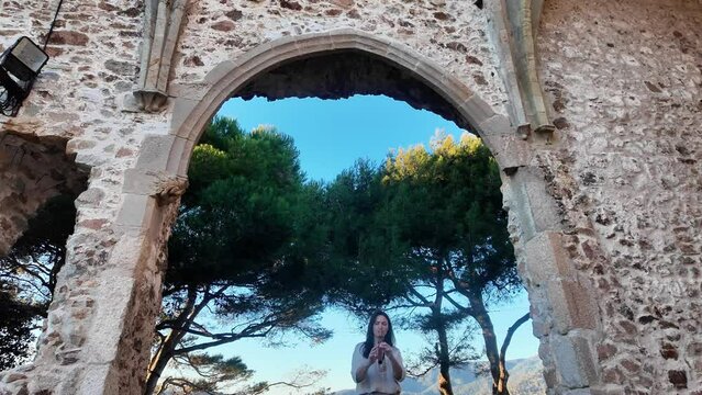 Woman playing flute in medieval ruins, with trees behind