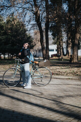 A joyful woman chats on her mobile phone while standing beside her vintage bicycle in a sunny park, embodying leisure and connectivity.