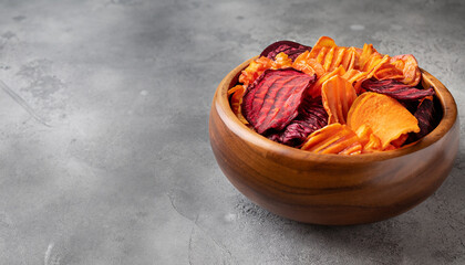 Wooden bowl with organic vegetable dehydrated beet, carrot and potato chips; gray stone table; copy space