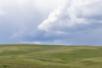 Fototapeta premium Scenic nature landscape of a hill covered in green grass with moody and dramatic storm clouds in the sky above it.