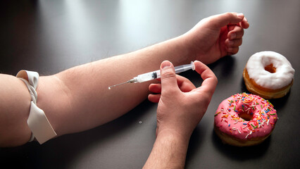 Man with syringe in hand injecting sugar from some donuts, sugar addiction. A sweet drug