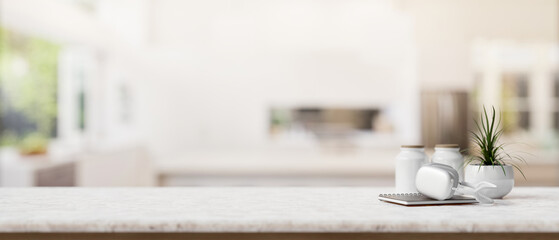 A book, headphones, a potted plant, and empty space on a tabletop in a modern white kitchen.