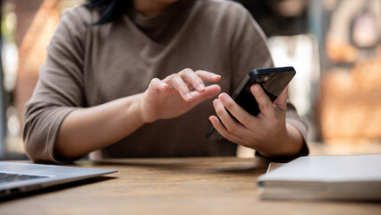 A cropped shot of an Asian woman responding to messages on her smartphone while sitting in a cafe.
