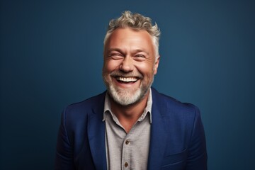 Portrait of a happy mature man laughing against a blue background.