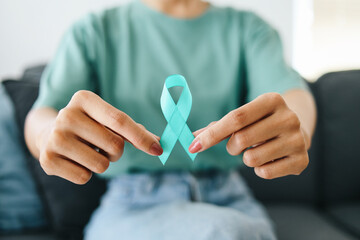 Close-up teal awareness ribbon holded by woman hands to support cancer survivor. Ovarian Cancer...