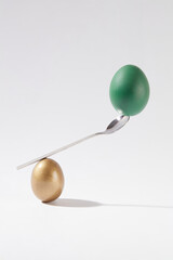A stack of a golden egg, a spoon and a green egg displayed over white background. For Easter Day concept. Easter Day is a Christian holiday commemorating the rebirth of Jesus Christ