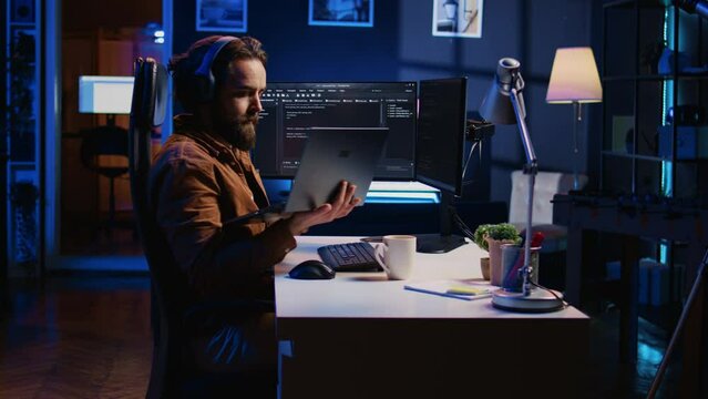 Engineer typing code in apartment office, using javascript programming language to develop software application. It admin using multimonitor desktop setup and notebook to finish tasks, camera B