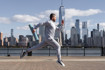 Man in sports suit training jogging running in Manhattan with fitness mat for workout outdoor