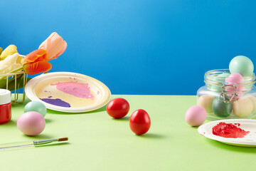 Easter concept with colorful Easter eggs displayed over blue background with a paintbrush, dishes of paint color and a basket of flowers. Easter, principal festival of the Christian church