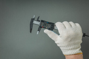 A gloved hand with an electronic caliper on a gray background.