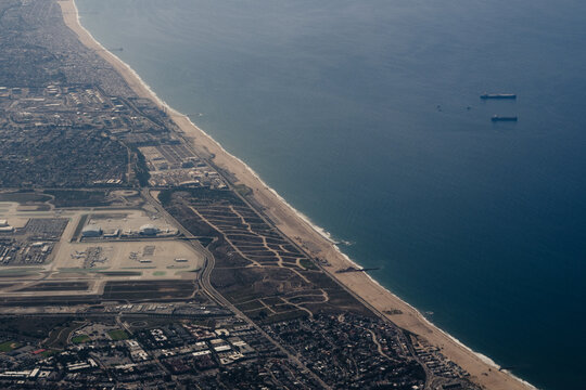 Aerial view of the shoreline of Los Angeles, with a view of the runways of Los Angeles International Airport (LAX) and large freight ships off the coast.
