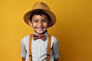 Portrait of a happy little boy wearing hat and suspenders against yellow background