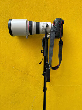 camera, camera on a tripod, camera with tripod in front of yellow rough and cracked wall, 
camera on yellow background