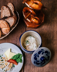 a wooden table with a bowl of soup, a plate of bread, and a basket of pretzels