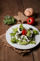 Colorful salad with cherry tomatoes, cucumber, and greens on a wooden table, toasted bread and fresh herbs complete the scene