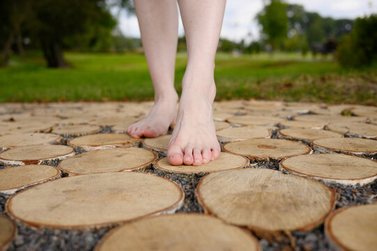 Woman walks barefoot along a massage tactile eco-path made of wooden saw cuts in the park, foot massage, prevention of flat feet. Relieving stress, depression, reflexology, unity with nature
