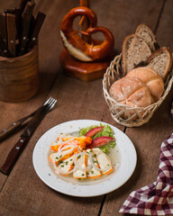Veggie platter on a wooden table with carrots, celery, onions, sauce, and pepper and bread basket on the side