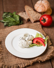 Tomato slices with cheese on a white plate, top-down view on a wooden table