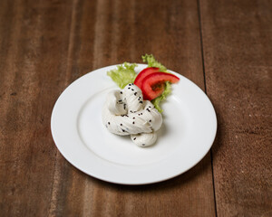 A white plate with a scoop of vanilla ice cream and a sliced tomato on a wooden table