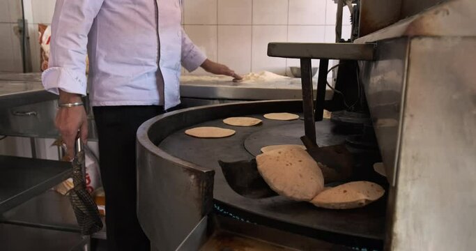 Supervising a high-tech chapati-making machine, a man effortlessly produces perfectly cooked, golden-brown chapatis with precision and expertise.