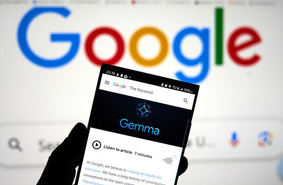 A hand holding a cellphone with Google Gemma logo over Google screen