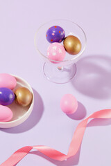 Easter Party concept with beautiful Easter eggs containing inside a ceramic dish and a wine glass. Pink ribbon featured. Easter Sunday is a religious Christian holiday