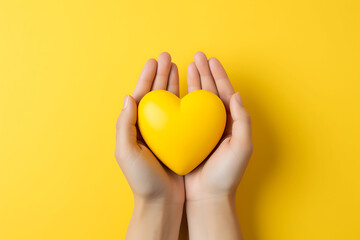 hands holding a yellow heart against a matching yellow background flat lay, yellow ribbons are...