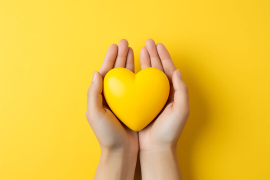 hands holding a yellow heart against a matching yellow background flat lay, yellow ribbons are associated with support for troops, suicide prevention, endometriosis awareness