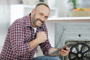man using tablet pc to fix a washing machine - obrazy, fototapety, plakaty